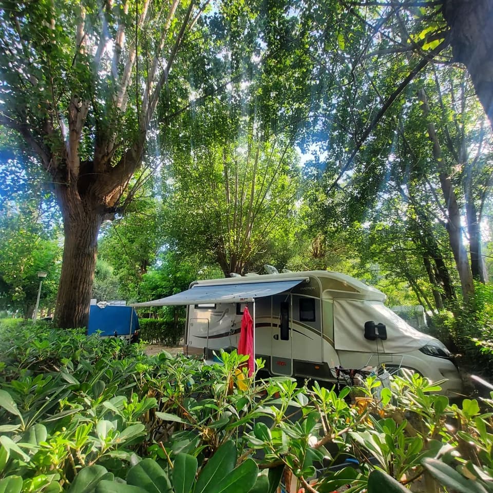 Un camper con veranda parcheggiato in una piazzola ombreggiata